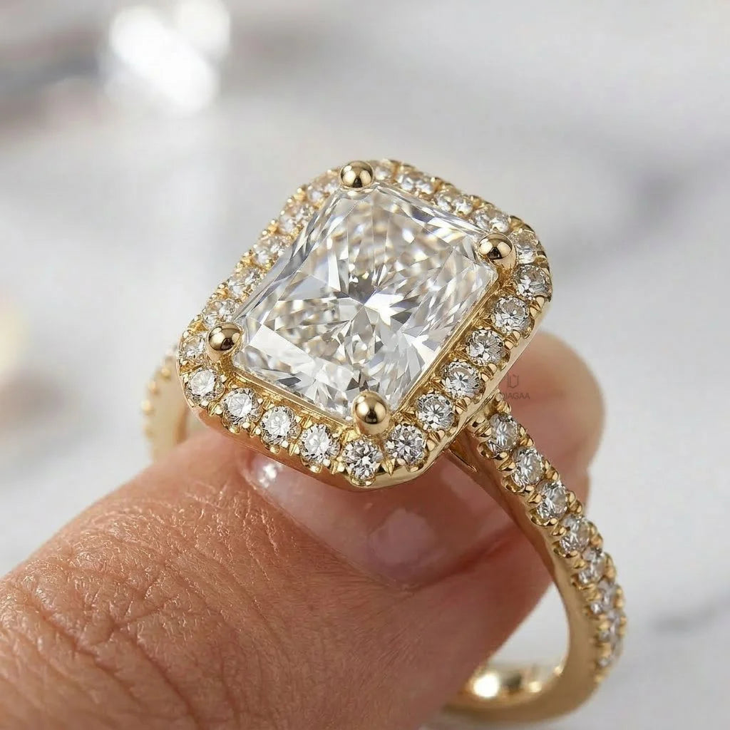 Close-up of fingers holding a yellow gold engagement ring featuring a large radiant-cut center diamond, a matching halo, and a pave set band.