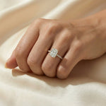 Woman's hand wearing a yellow gold radiant cut diamond engagement ring with a round diamond pavé band on beige silk background.