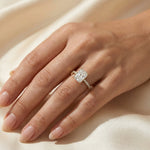 Woman's hand wearing a 14k yellow gold radiant cut diamond engagement ring with a round diamond pavé band on beige silk background.