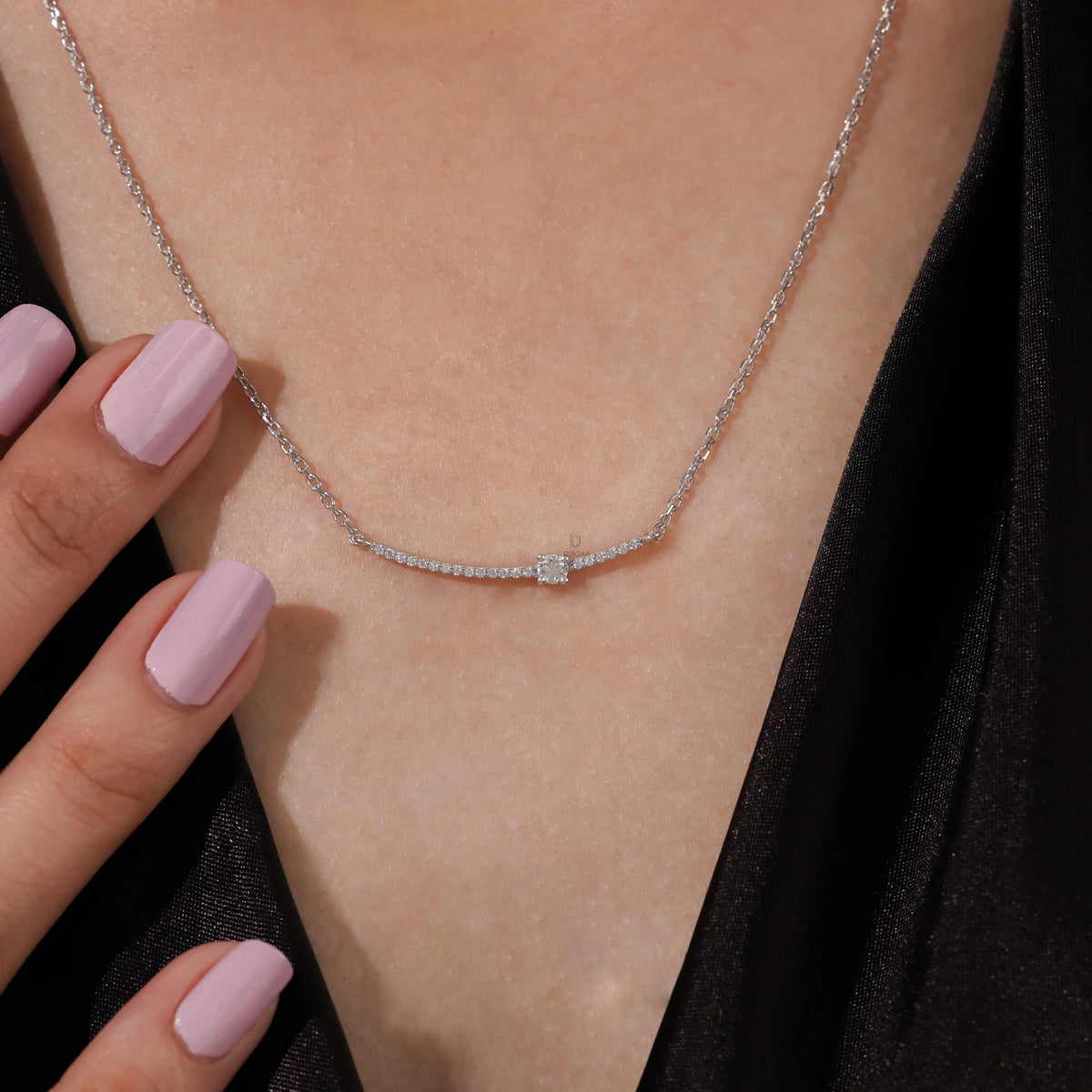 Woman wearing a delicate Round diamond necklace with a prong and pave-set solitaire curved bar in white gold.