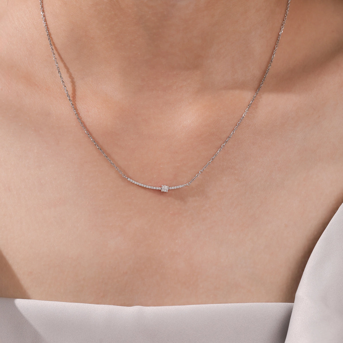 Woman wearing a delicate Round diamond necklace with a prong and pave-set solitaire curved bar in white gold.