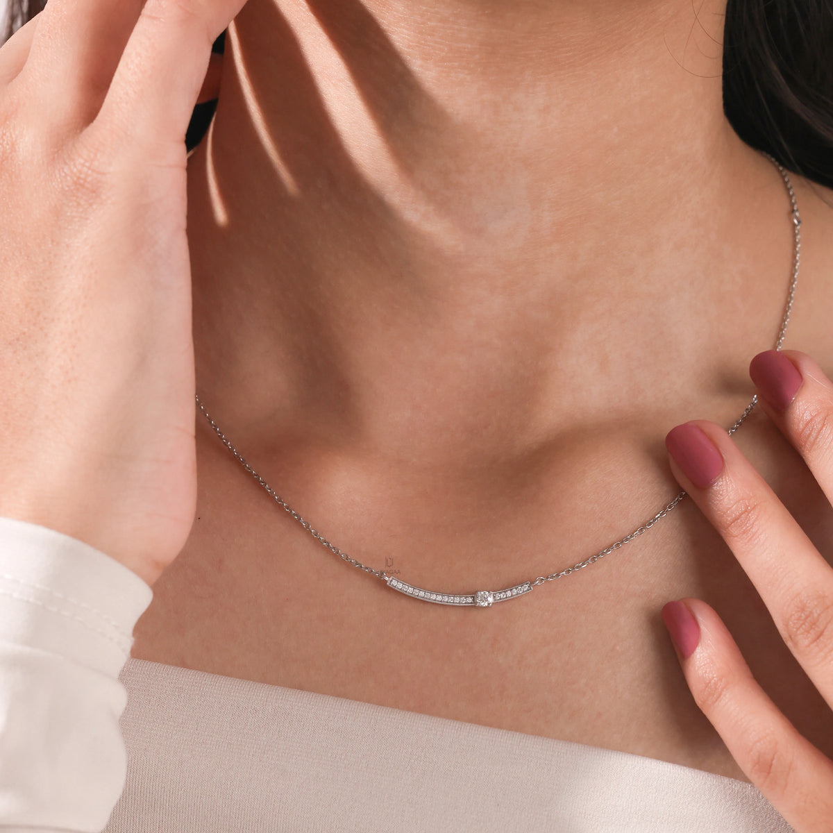 Woman wearing a delicate Round diamond necklace featuring a prong and pave-set solitaire curved bar in white gold.