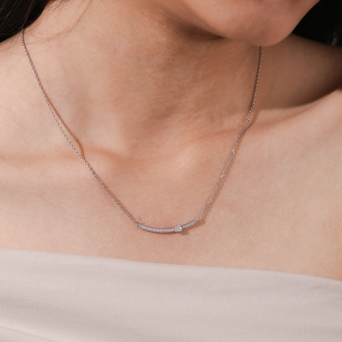 Woman wearing a delicate Round diamond necklace featuring a prong and pave-set solitaire curved bar in white gold.