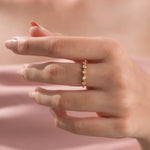 Close-up of a delicate gold ring with five bezel-set round diamonds worn on a woman's ring finger.