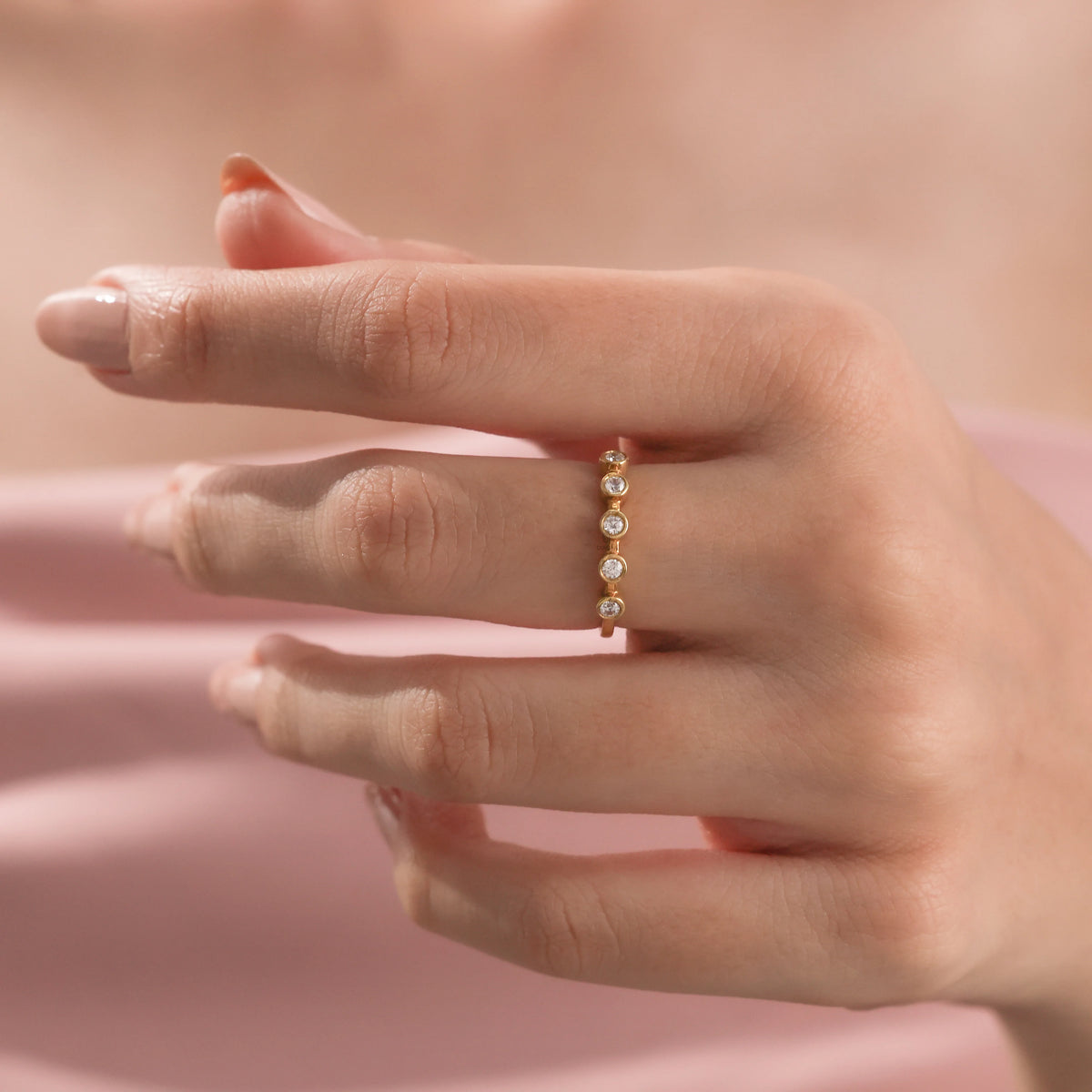 Close-up of a delicate gold ring with five bezel-set round diamonds worn on a woman's ring finger.