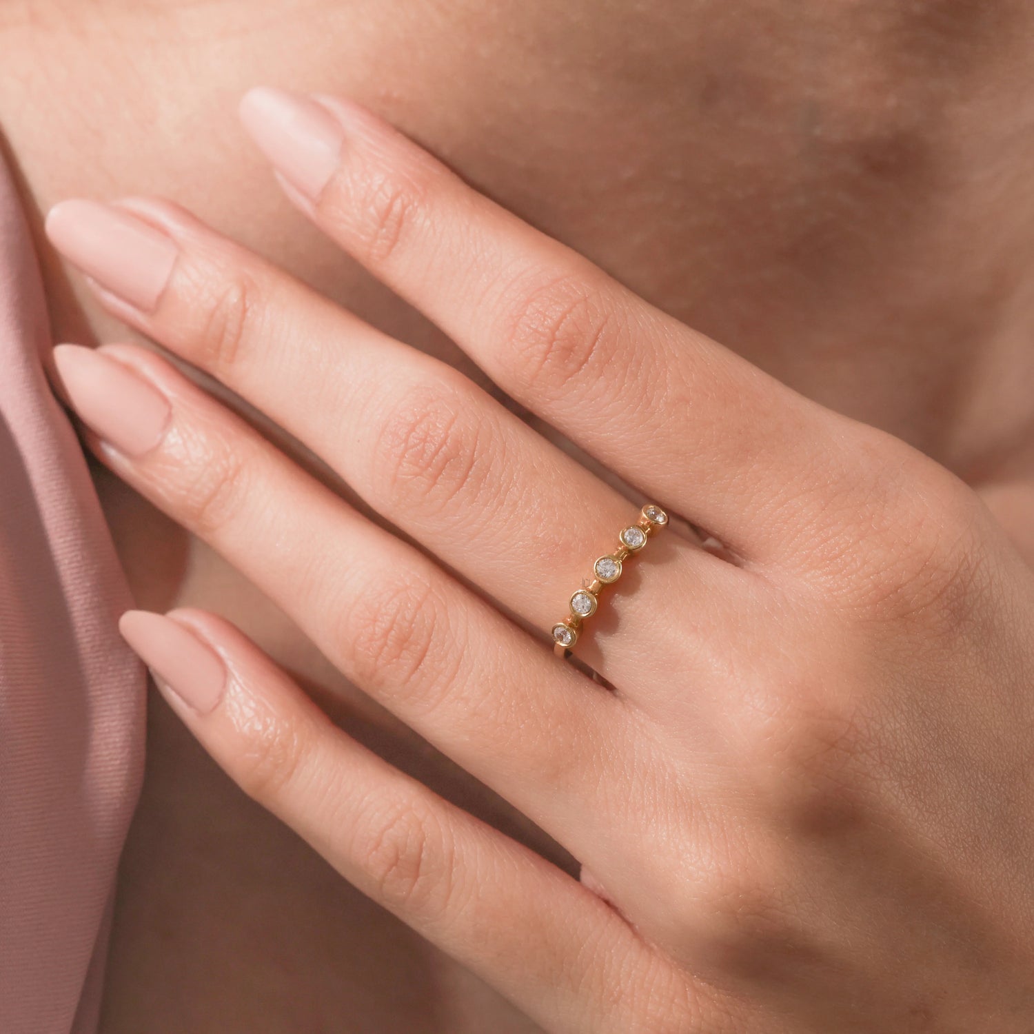 Woman wearing a delicate yellow gold 5-stone diamond ring featuring round bezel-set stones on her ring finger.