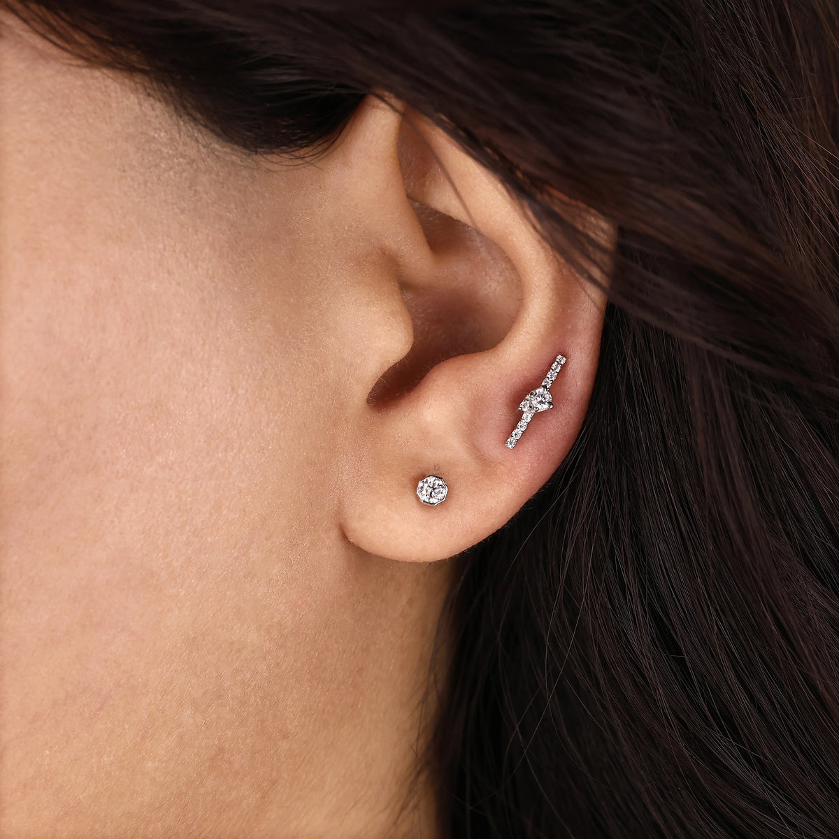 A single round diamond stud earring set in a 14K yellow gold bezel setting, shown worn on an earlobe.