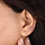 A single round diamond stud earring set in a 18K yellow gold bezel setting, shown worn on an earlobe.