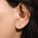 A single round diamond stud earring set in a 10K yellow gold bezel setting, shown worn on an earlobe.