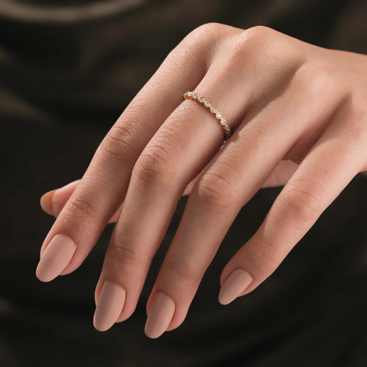 A delicate yellow gold full eternity diamond band showing a repeating round disc profile on a hand for a minimal bridal look.