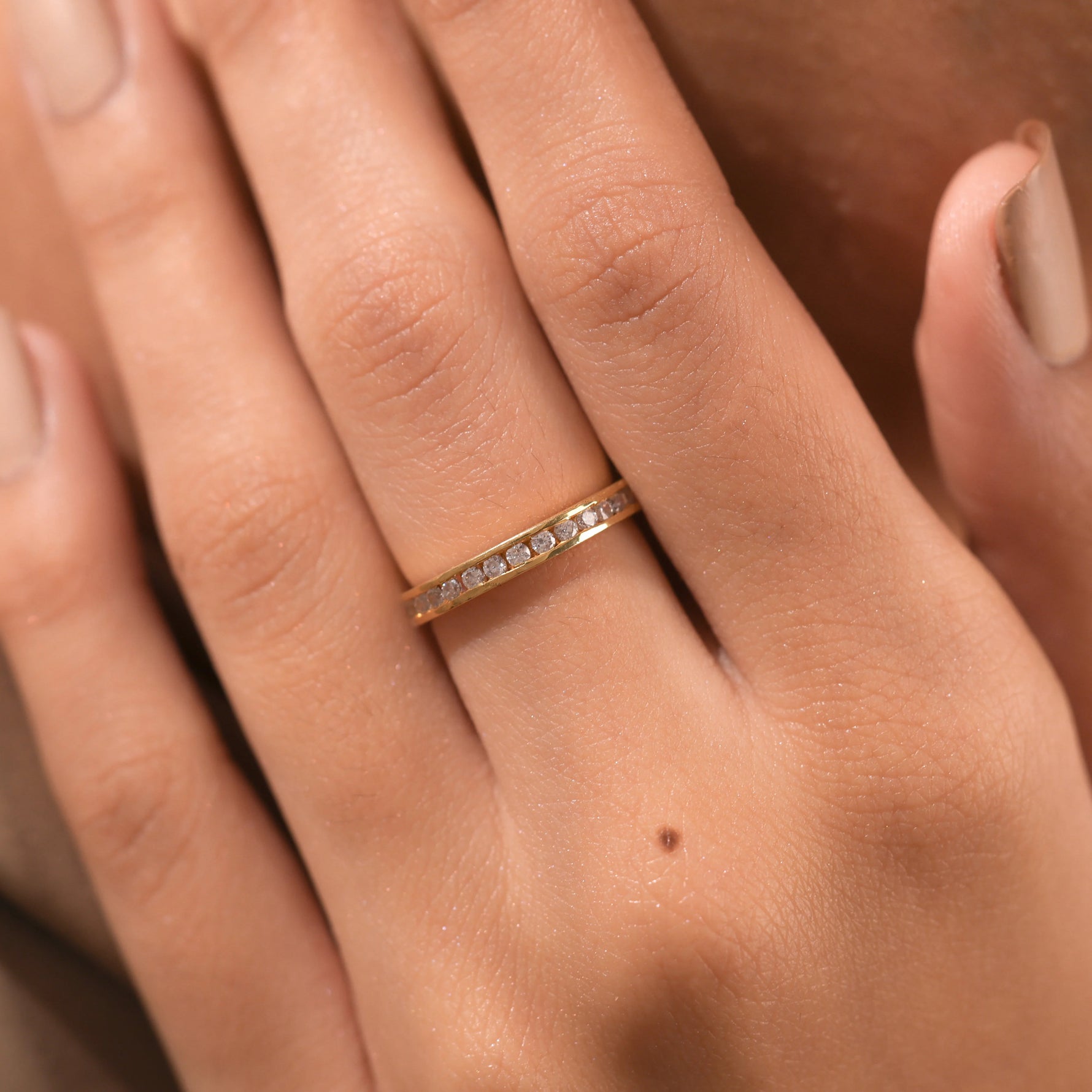 Elegant yellow gold channel-set diamond wedding band worn on a finger, showcasing a seamless row of brilliant diamonds.