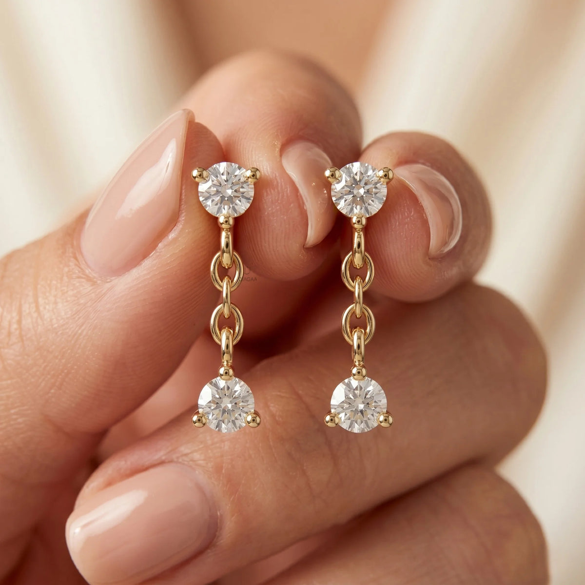 A pair of yellow gold diamond drop earrings featuring round-cut stones connected by gold links, held in fingers. Elegant fine jewelry for women.