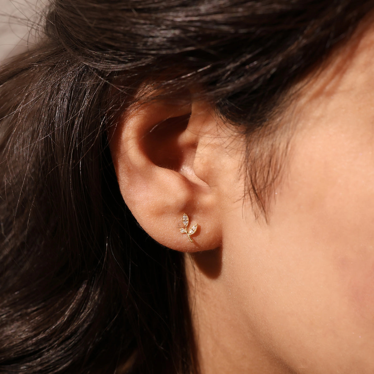 Close-up model photo showcasing a dainty yellow gold leaf stud earring worn on the earlobe, highlighting its small botanical design earring. 