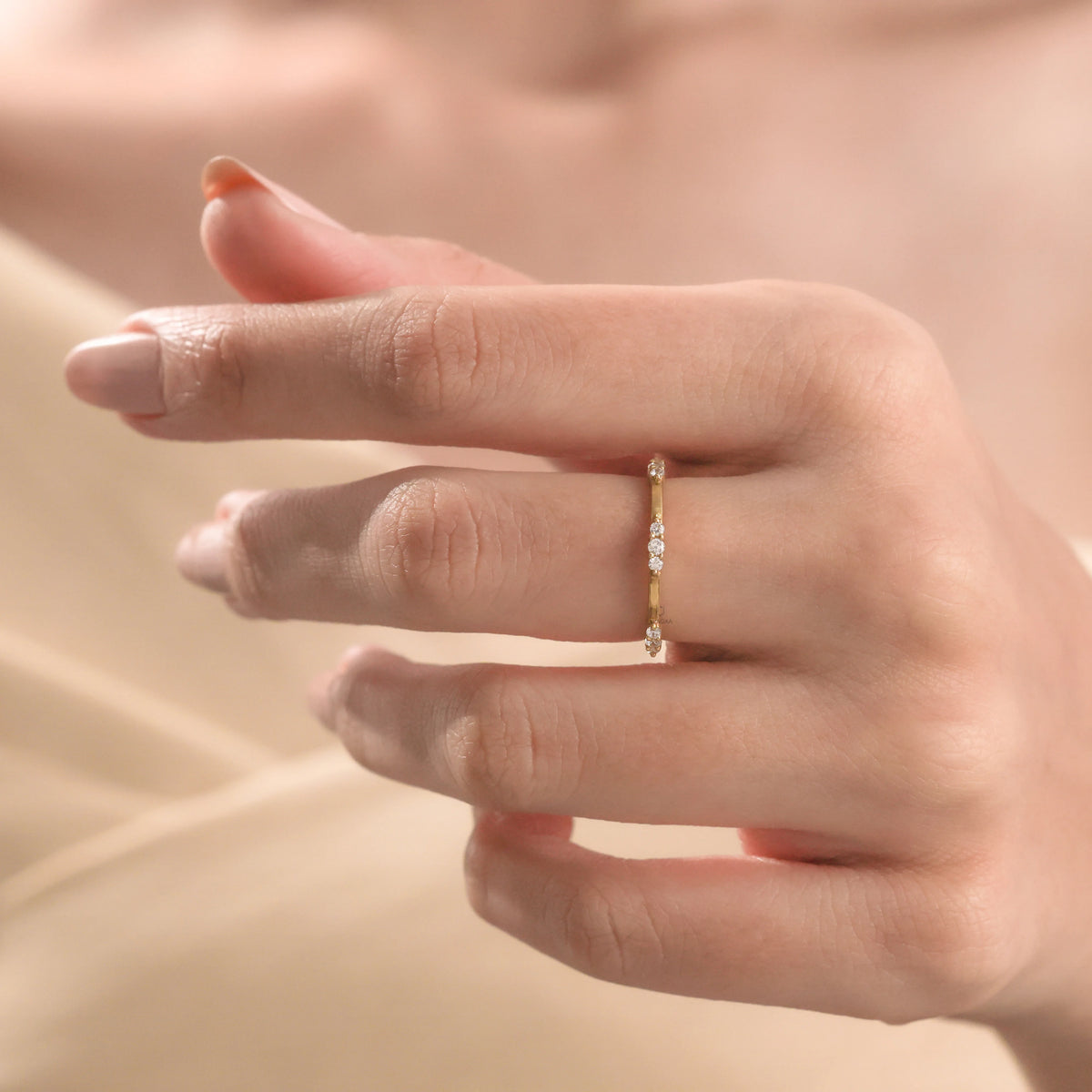 A dainty yellow gold diamond stackable wedding band worn on a hand, featuring a subtle, multi-stone sparkling design ideal for a classic engagement look.