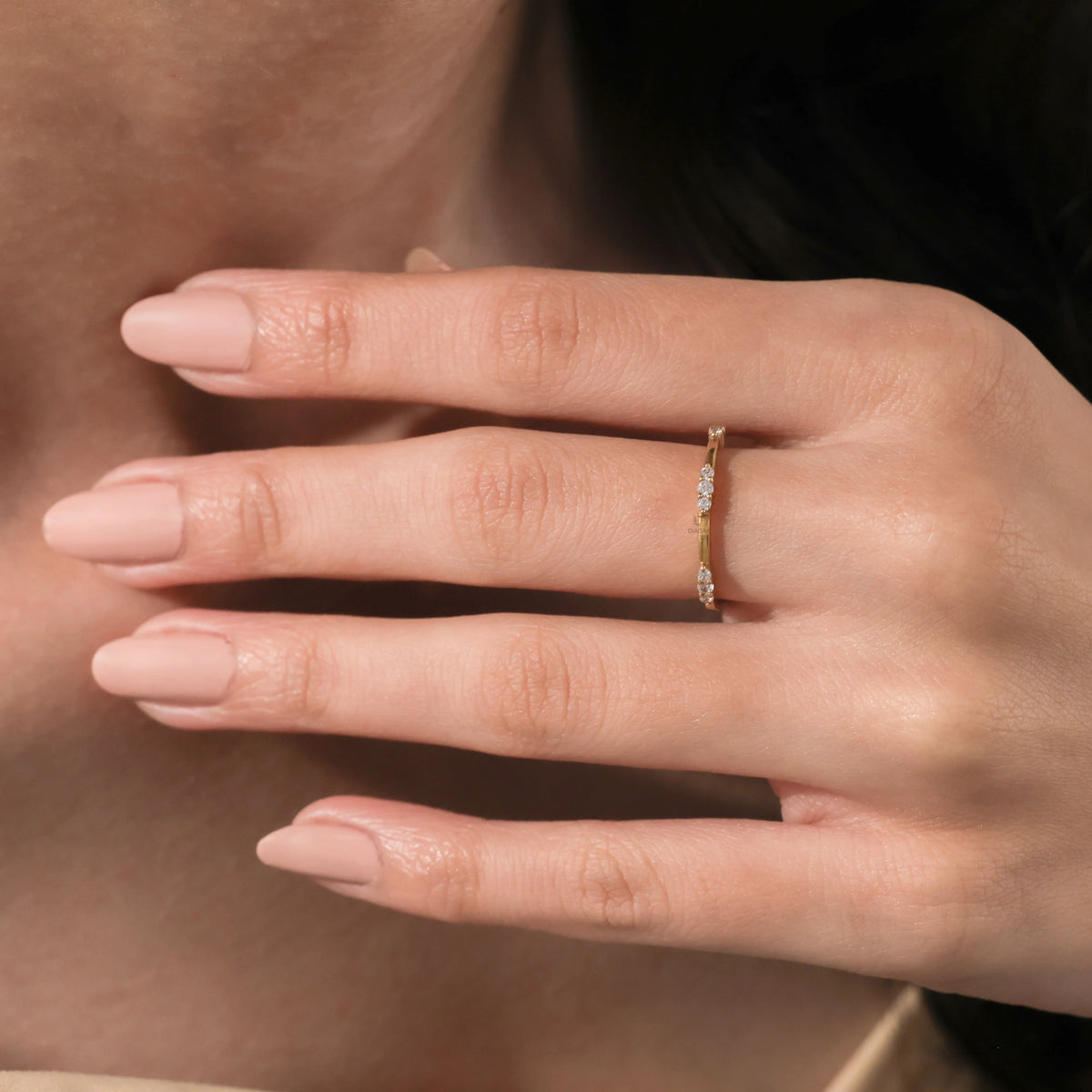Close-up of a hand with a nude manicure wearing a delicate yellow gold diamond band with cluster settings.