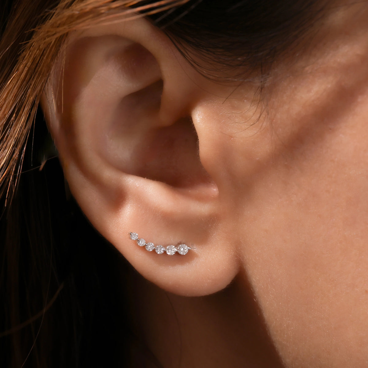 Curved climber-style round diamond stud earring styled along the earlobe, featuring aprong-setting and available in  14K yellow gold