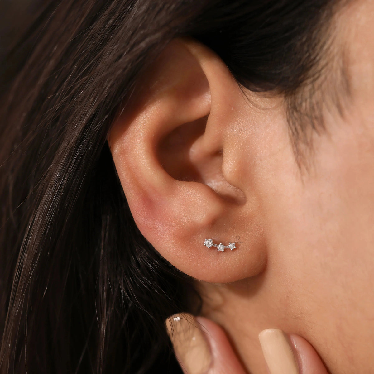 White gold three stone diamond climber earring worn on an ear lobe to demonstrate everyday scale, curved cluster design styling, and real-life fit.