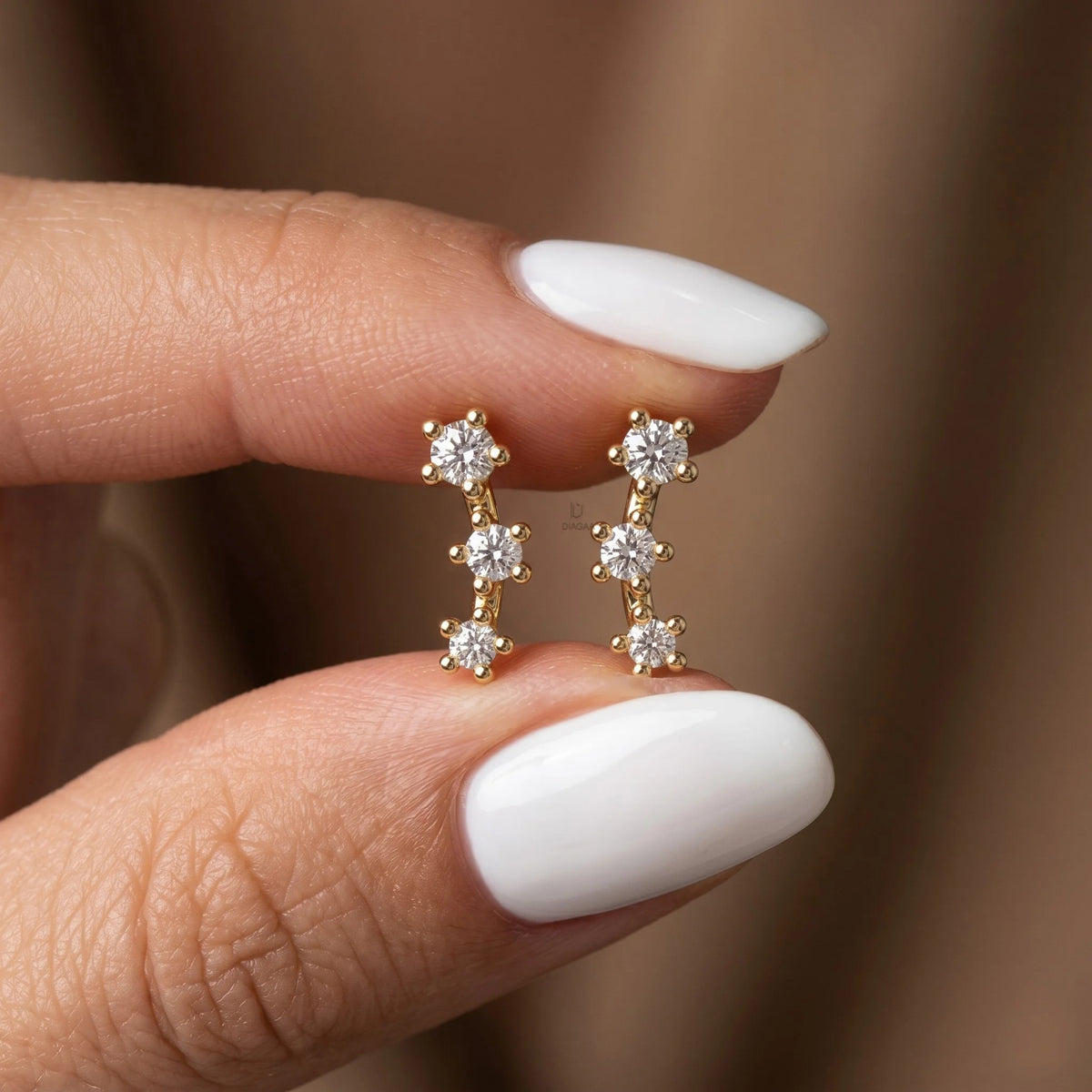 Yellow gold three stone diamond climber earrings held by a hand to demonstrate everyday scale, brilliant prong setting details, and real life fit.