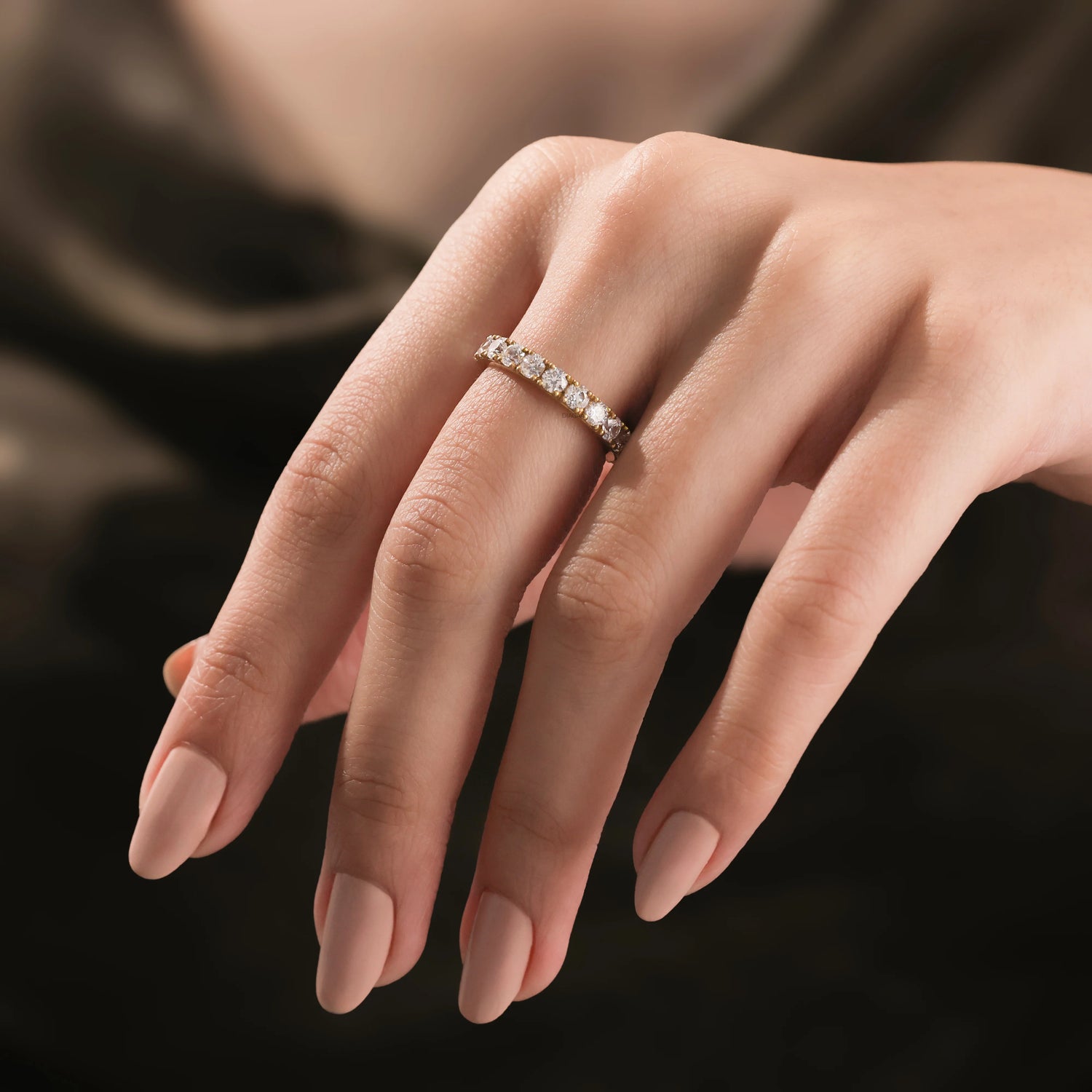 round Diamond eternity band ring on a woman's hand, featuring a row of round diamonds set in a delicate yellow gold band.