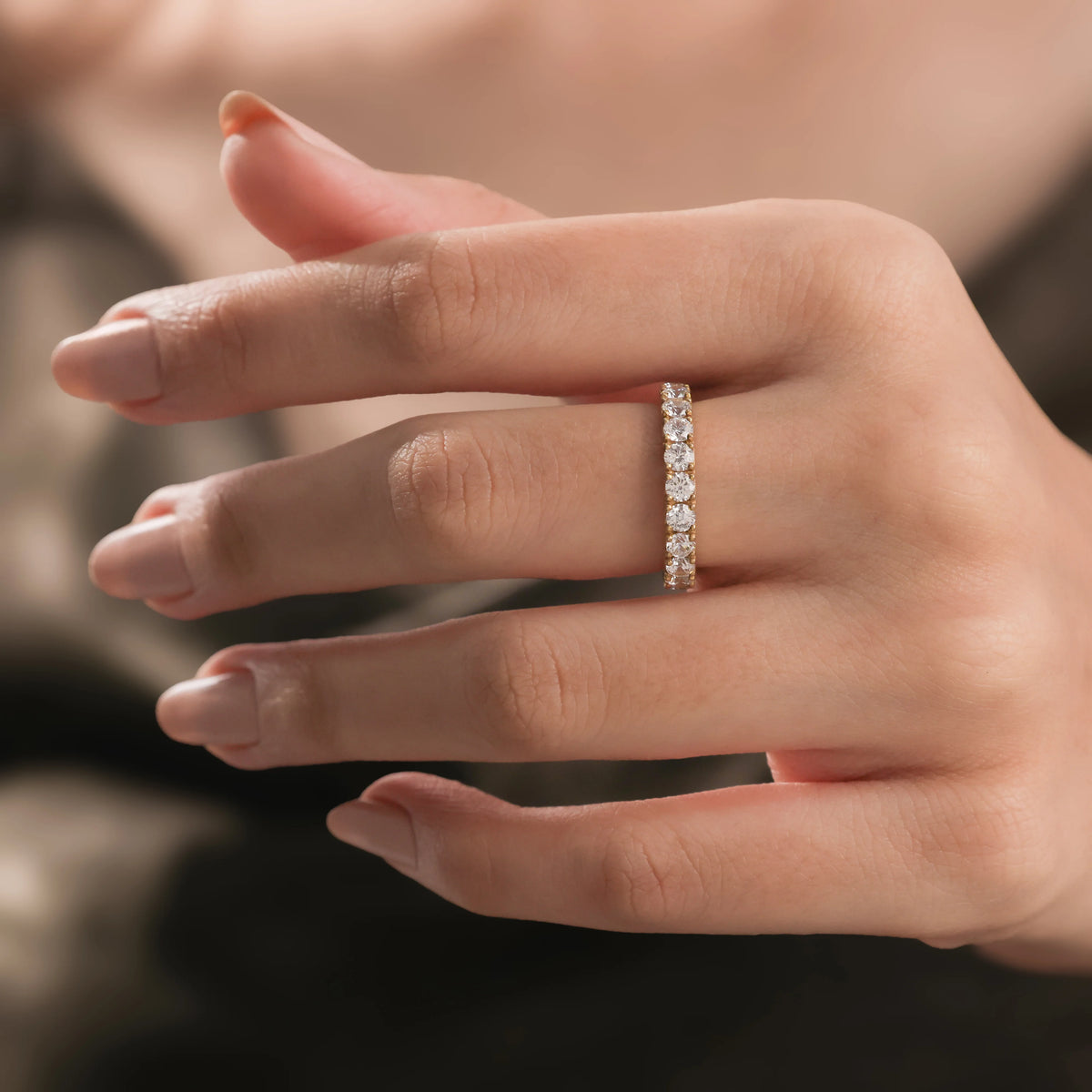 Elegant woman wearing a sparkling yellow gold round diamond wedding ring, resting her hand lightly on her chin.