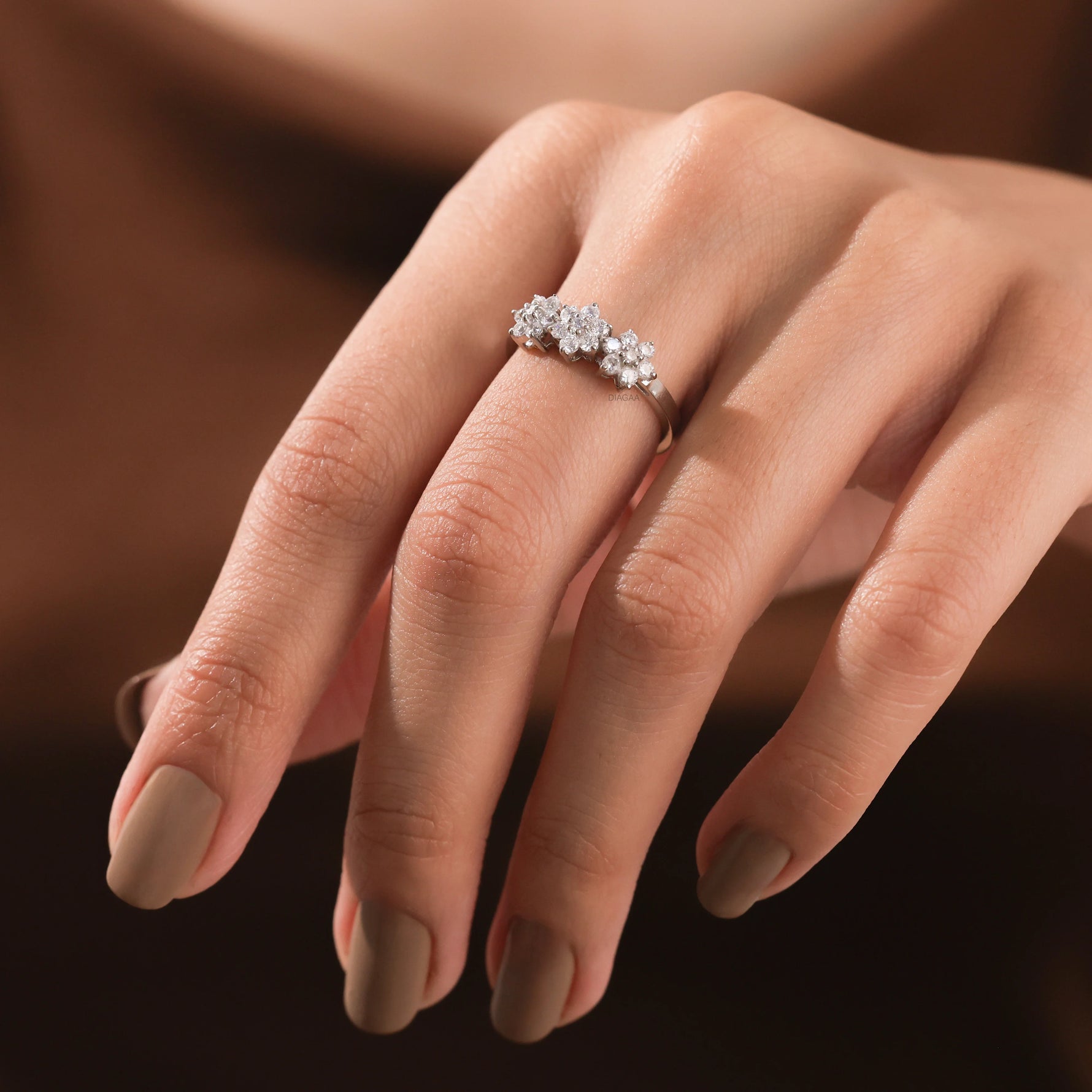 elicate white gold round diamond cluster ring with an intricate three-flower motif worn on a woman's finger.