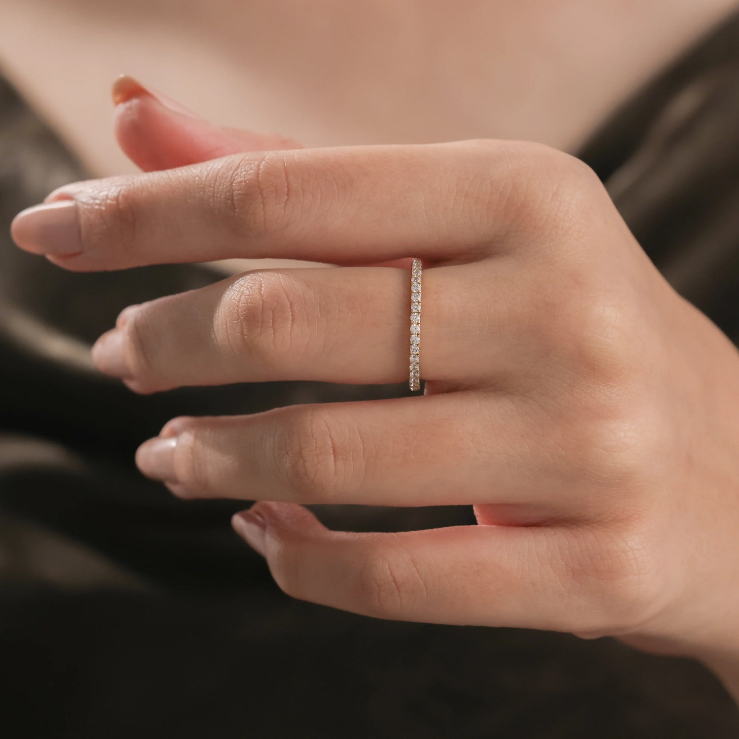 Close-up of a woman's hand wearing a delicate yellow gold diamond pave ring on her middle finger. Beautiful fine jewelry reference