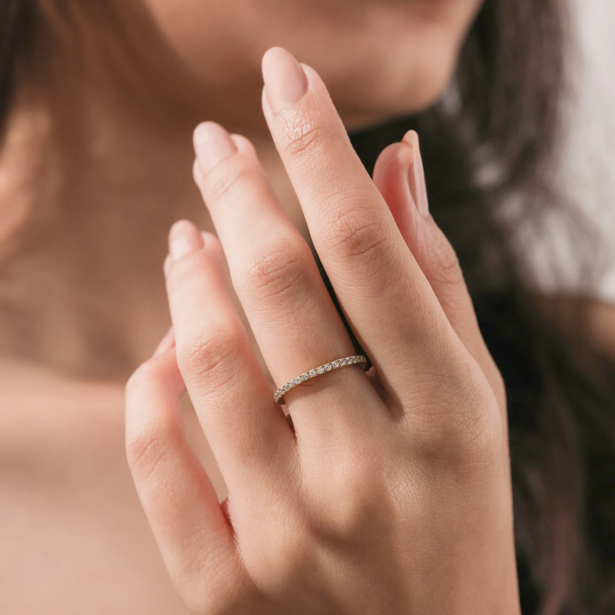 14k yellow gold round diamond eternity stackable ring worn on a middle finger against a soft brown background. Perfect wedding band inspiration.