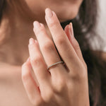 14k yellow gold round diamond eternity stackable ring worn on a middle finger against a soft brown background. Perfect wedding band inspiration.