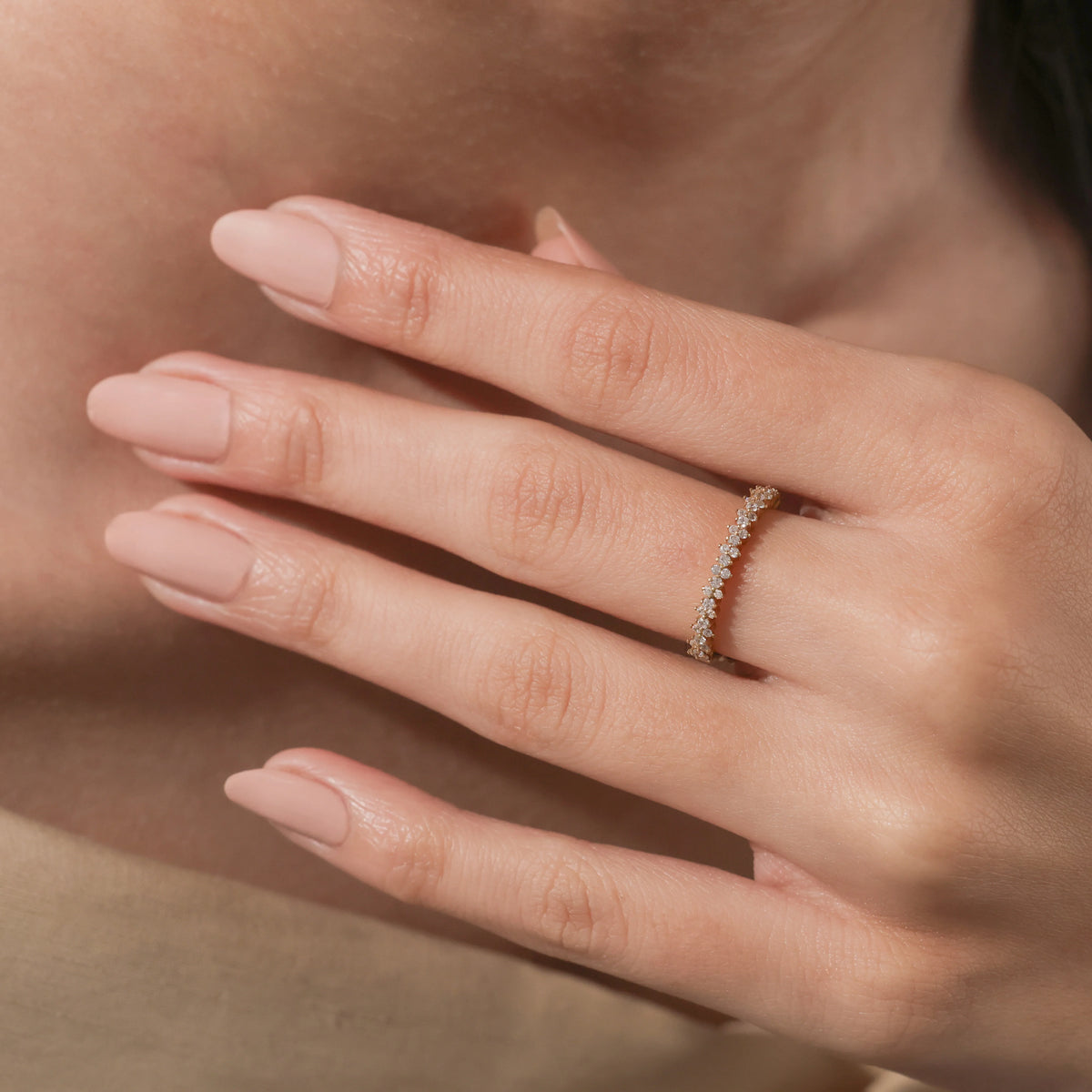 Woman's hand wearing a delicate yellow gold diamond eternity band on her ring finger, showcasing a staggered cluster setting.