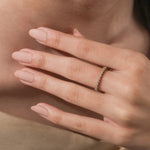 Woman's hand wearing a delicate yellow gold diamond eternity band on her ring finger, showcasing a staggered cluster setting.
