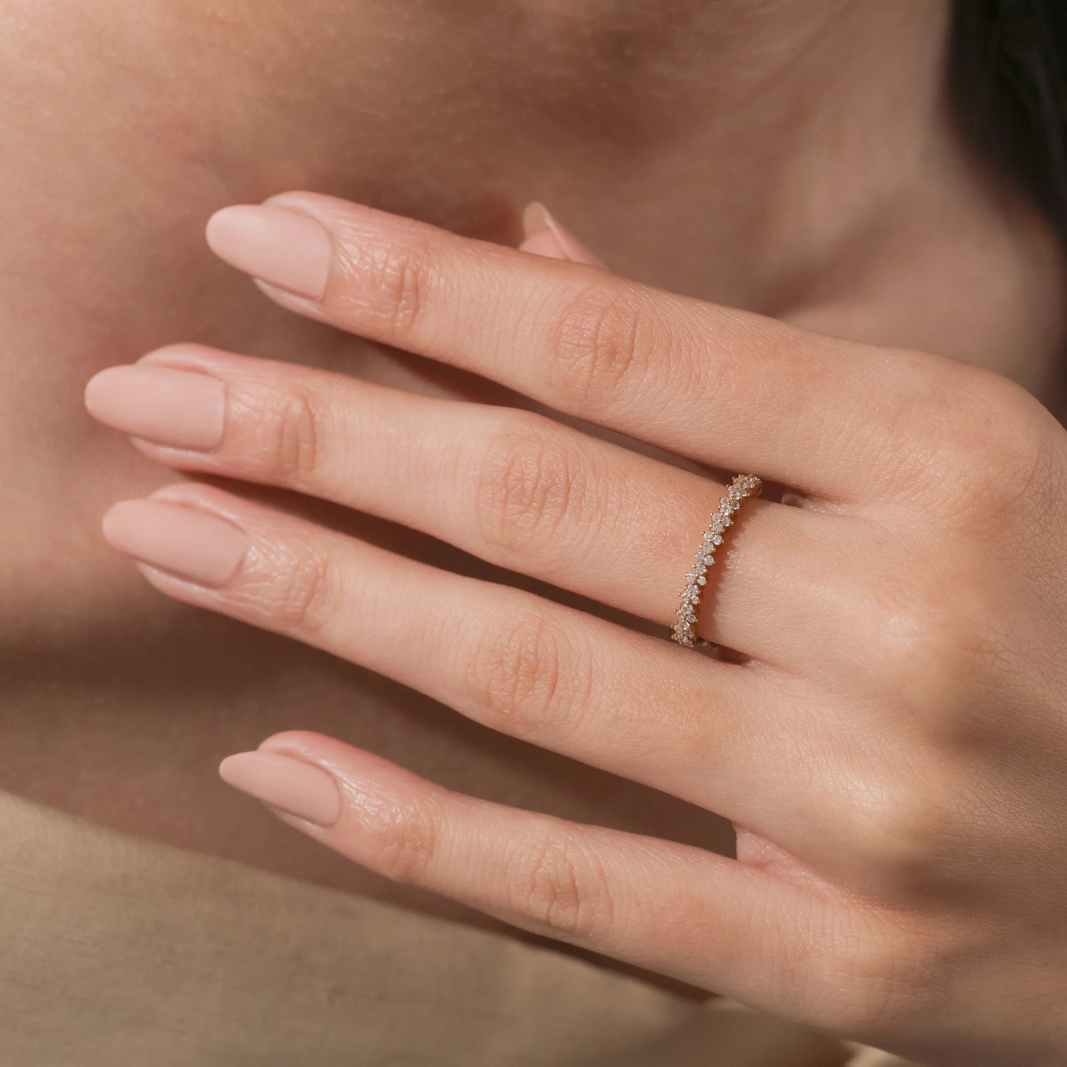 Woman's hand wearing a delicate yellow gold diamond eternity band on her ring finger, showcasing a staggered cluster setting.