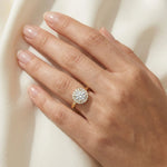 Solitaire round-cut diamond engagement ring with a pavé halo setting in yellow gold, modeled on a hand.