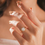 Solitaire round-cut diamond engagement ring with a pavé halo setting in 14k yellow gold, modeled on a hand.