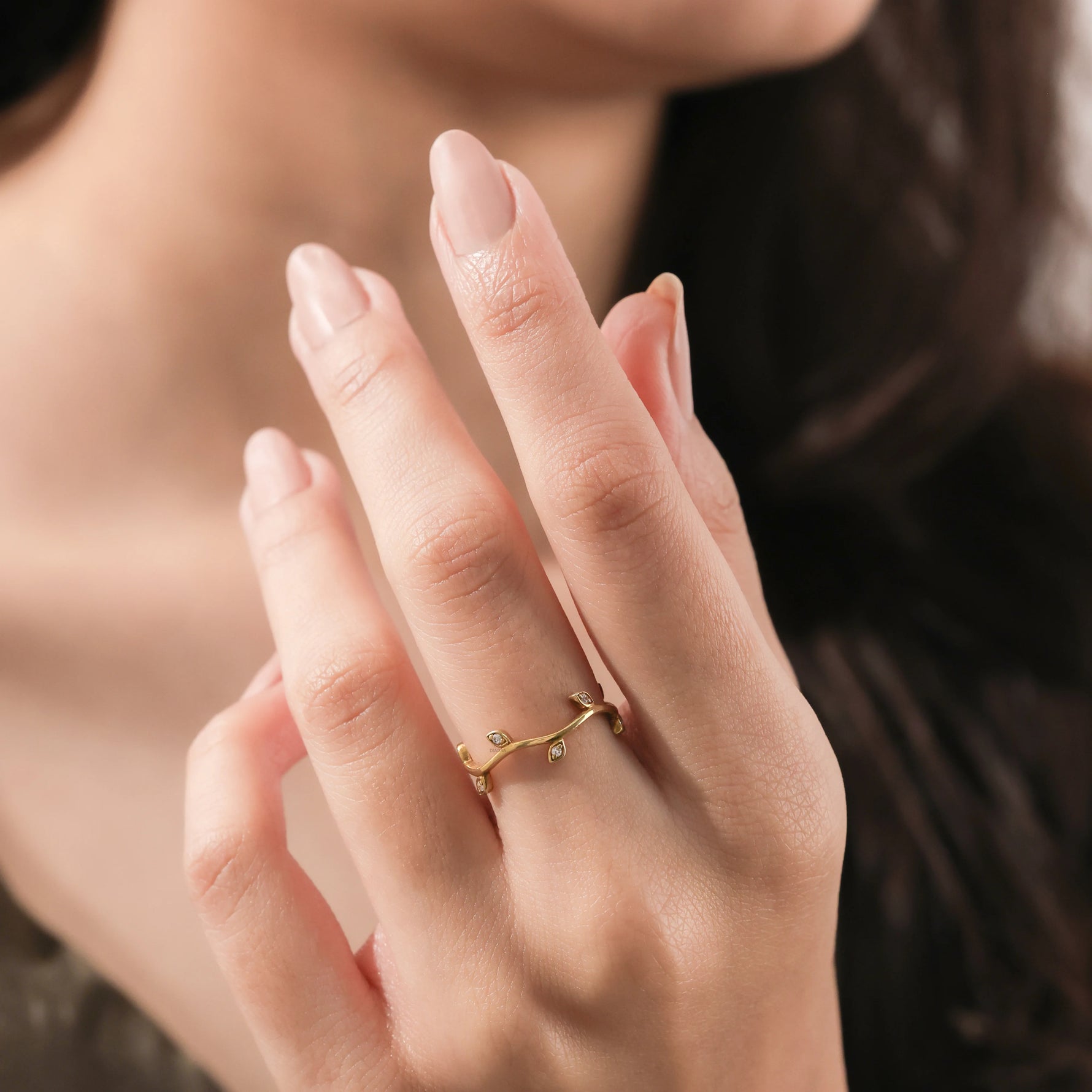 Close-up of a yellow gold diamond leaf ring on a woman's hand. Minimalist botanical wedding band and delicate twig jewelry.