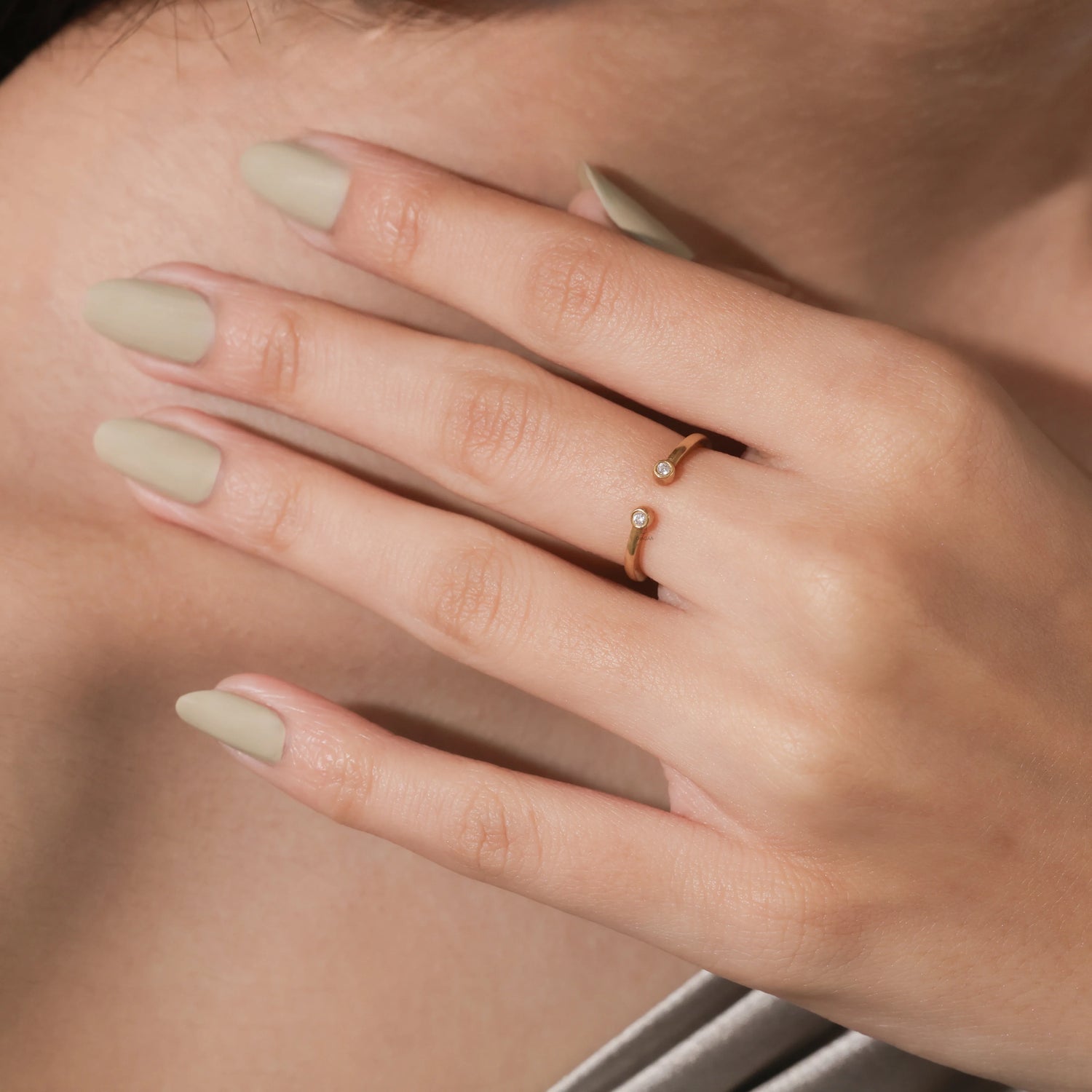 A delicate open yellow gold cuff ring featuring two small round cut bezel-set diamonds worn on a woman's middle finger.