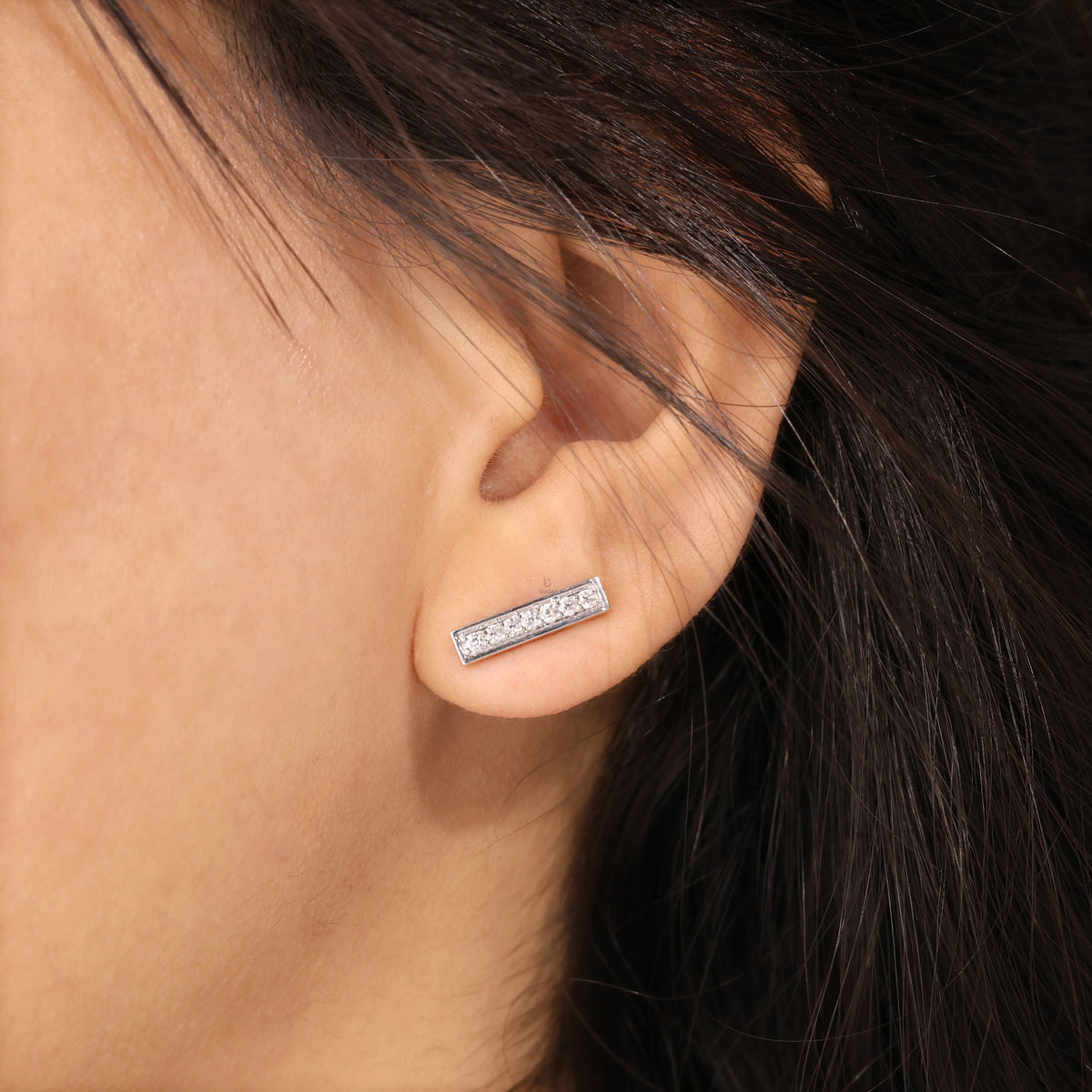 Vertical bar style round diamond stud earring styled on earlobe, featuring a sparkling pave setting in 14K white gold.
