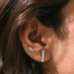 Vertical bar style round diamond stud earring styled on earlobe, featuring a sparkling pave setting in 10K white gold.