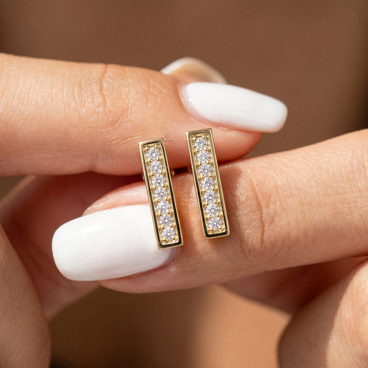 Pair of bar style round diamond stud earring designs held in hand, crafted in yellow gold with a brilliant pave setting