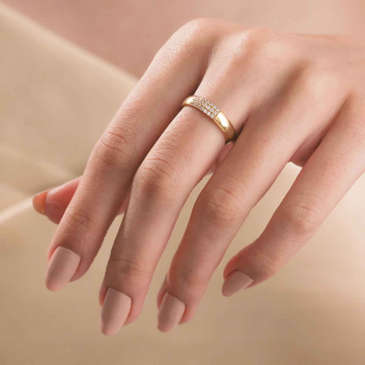 Woman wearing a thick yellow gold diamond band ring with a three-row pavé setting on her middle finger.