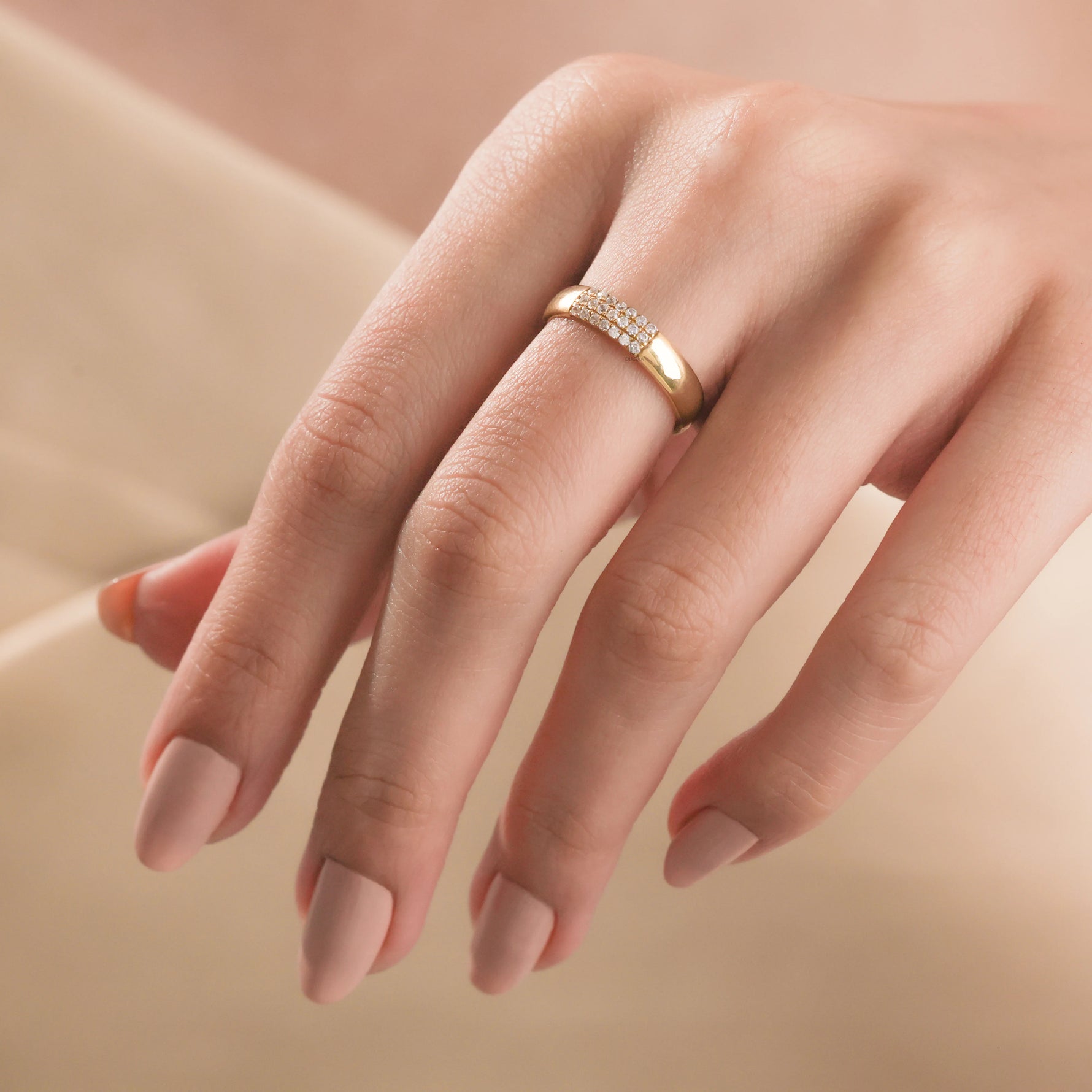 Woman wearing a thick yellow gold diamond band ring with a three-row pavé setting on her middle finger.