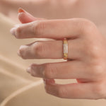 Elegant minimalist yellow gold band ring featuring a rectangular block of small pavé diamonds, worn on a finger against a soft beige silk backdrop.