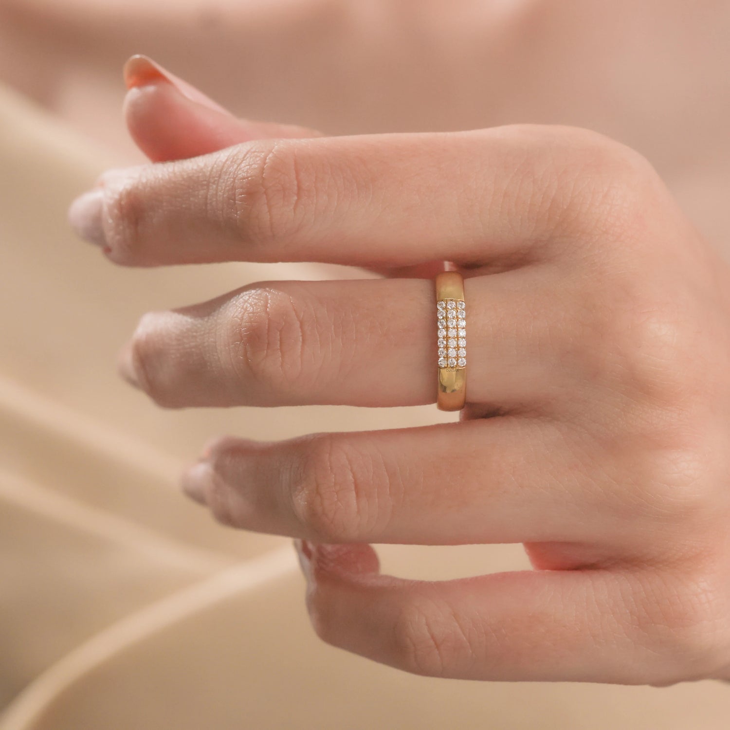 Elegant minimalist yellow gold band ring featuring a rectangular block of small pavé diamonds, worn on a finger against a soft beige silk backdrop.