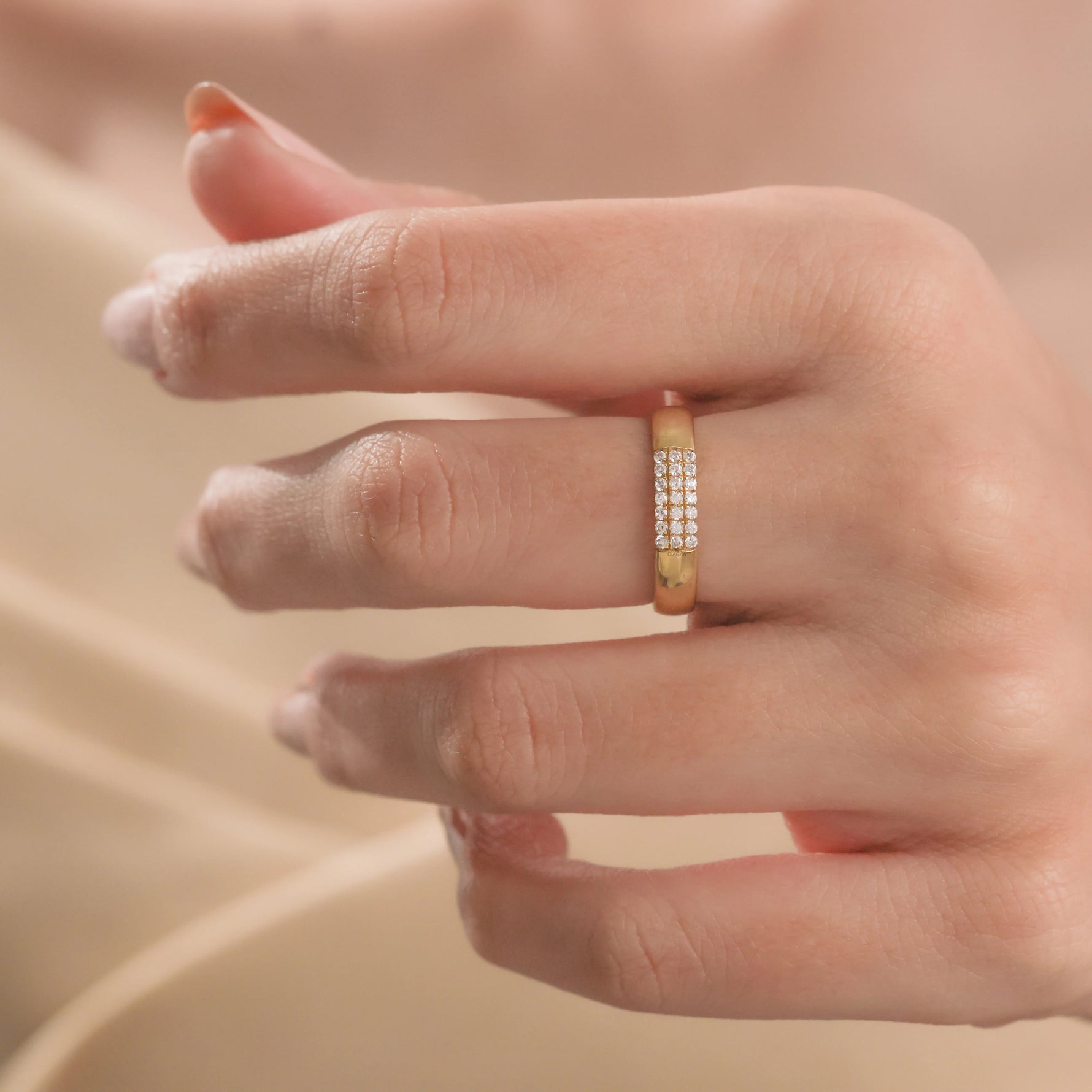 Elegant minimalist yellow gold band ring featuring a rectangular block of small pavé diamonds, worn on a finger against a soft beige silk backdrop.