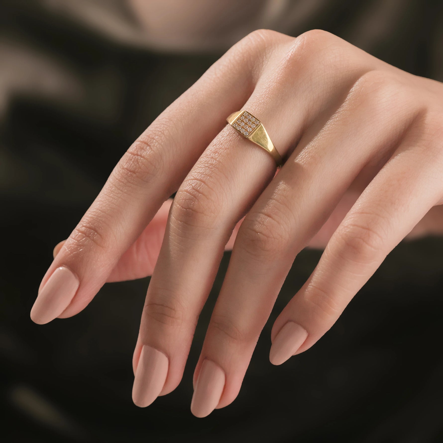 Model wearing a yellow gold square signet ring on her pinky finger, showcasing a minimalist diamond pave ring look.