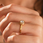 Close-up view of a woman wearing a yellow gold bezel set diamond engagement ring on her finger.