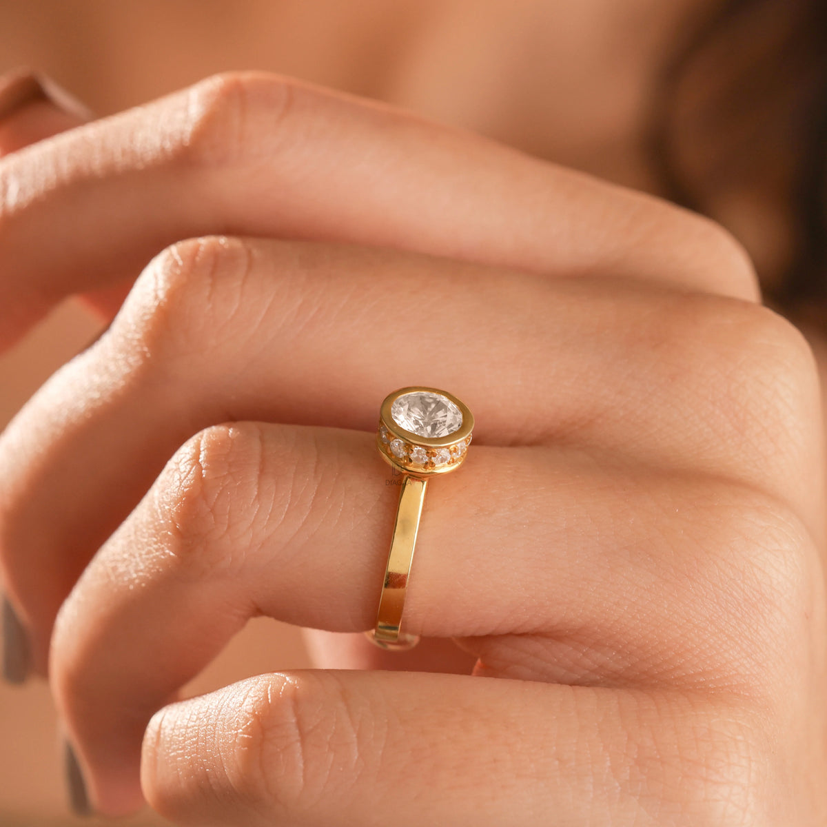 Close-up view of a woman wearing a yellow gold bezel set diamond engagement ring on her finger.