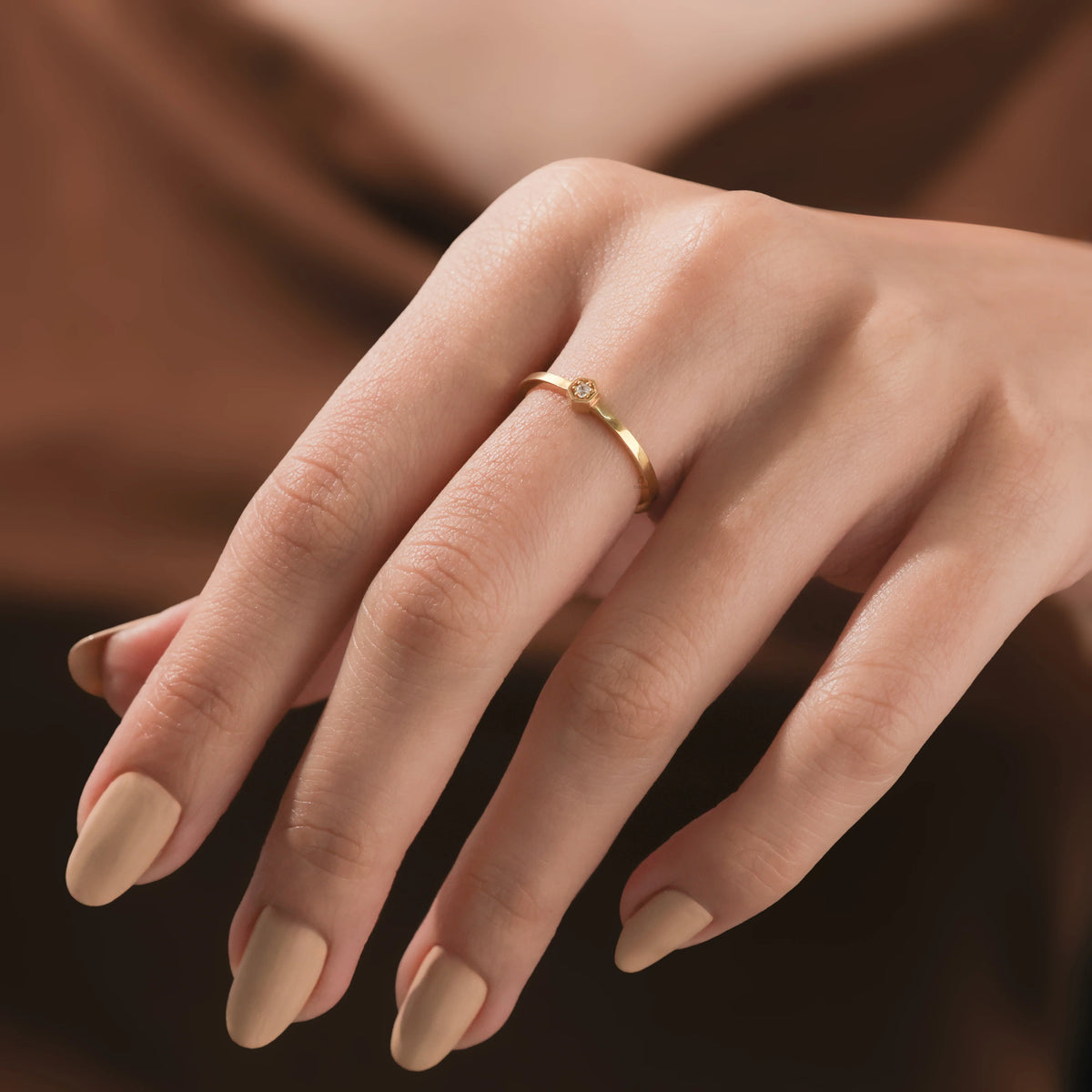 Close-up of a woman's hand wearing a dainty gold ring with a small hexagon-set round diamond wedding band  