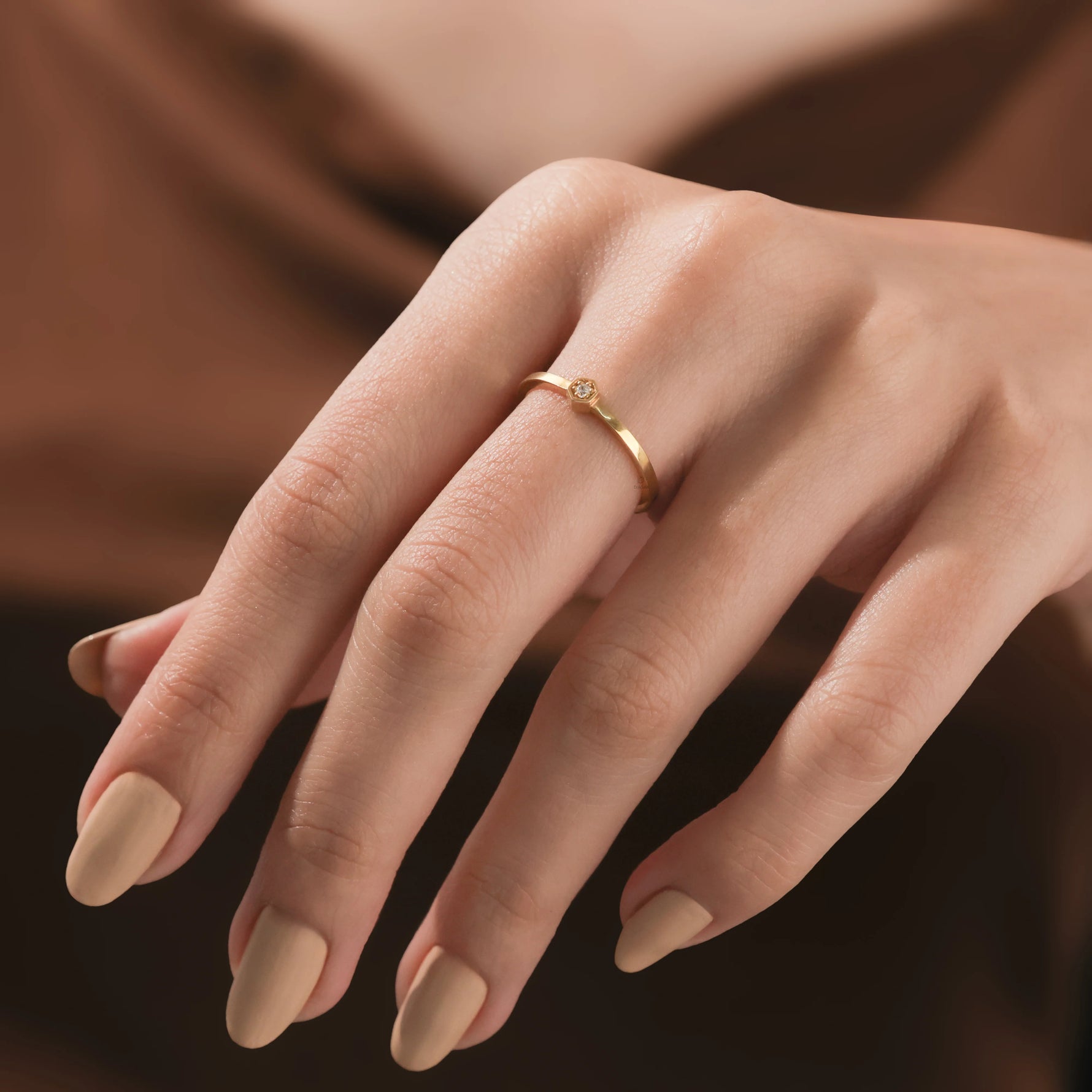 Close-up of a woman's hand wearing a dainty gold ring with a small hexagon-set round diamond wedding band  