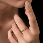 Yellow gold geometric ring featuring a small round diamond in a hexagon setting worn on a woman's hand.