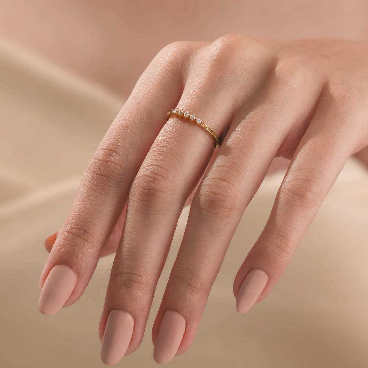 A woman wearing a dainty yellow gold stacking ring featuring a linear cluster of five small round diamonds.
